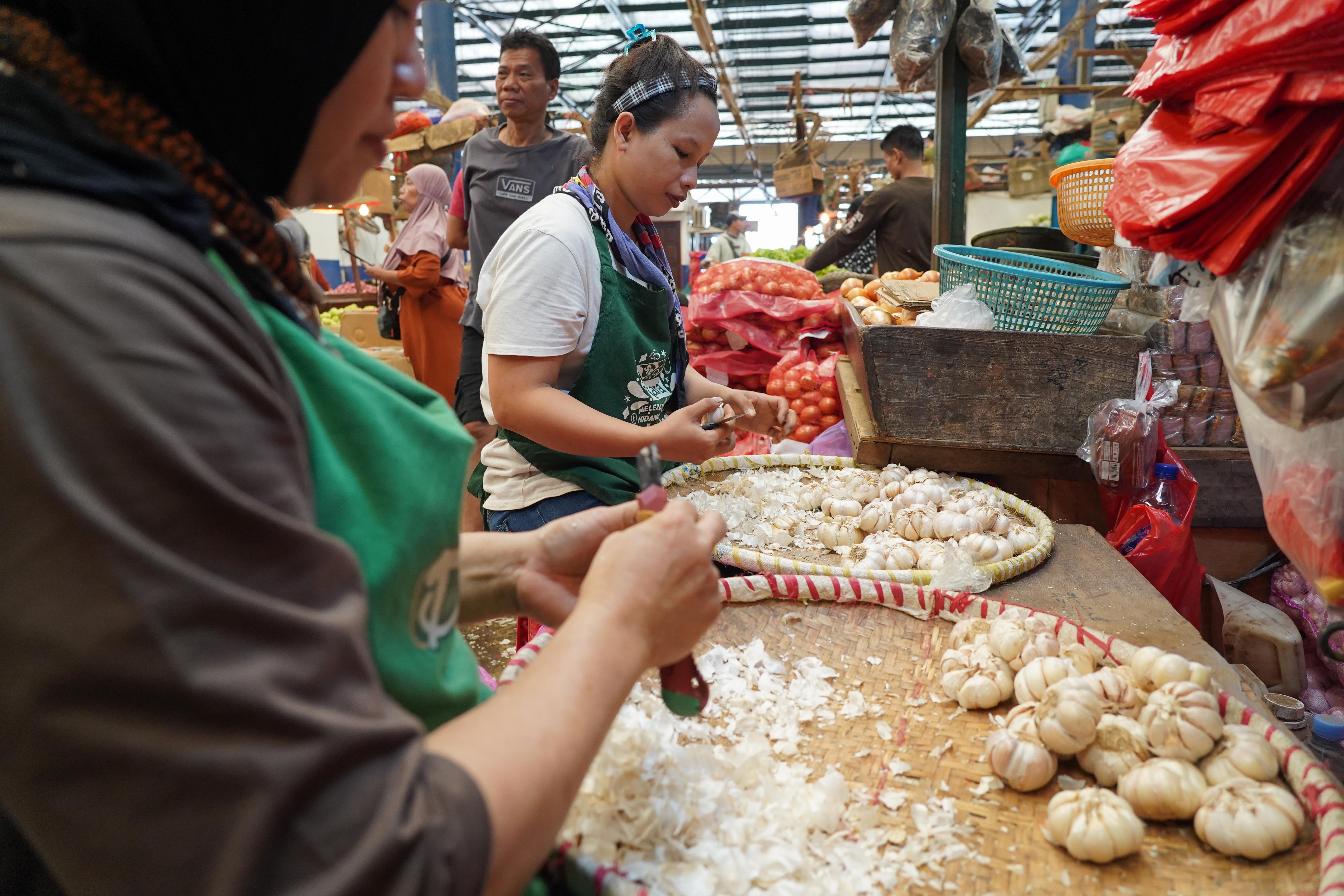 Pekerja mengupas kulit bawang putih impor yang dijual di Pasar Induk Kramat Jati, Jakarta, Selasa (14/7/2026). Berdasarkan pemantauan Indeks Perkembangan Harga (IPH), rata-rata harga bawang putih secara nasional kini mencapai Rp 42.611 per kilogram atau sudah berada jauh di atas Harga Acuan Penjualan (HAP) konsumen. Kenaikan ini disebabkan oleh melemahnya nilai tukar rupiah terhadap dolar Amerika Serikat (AS) dan meningkatnya biaya logistik internasional.