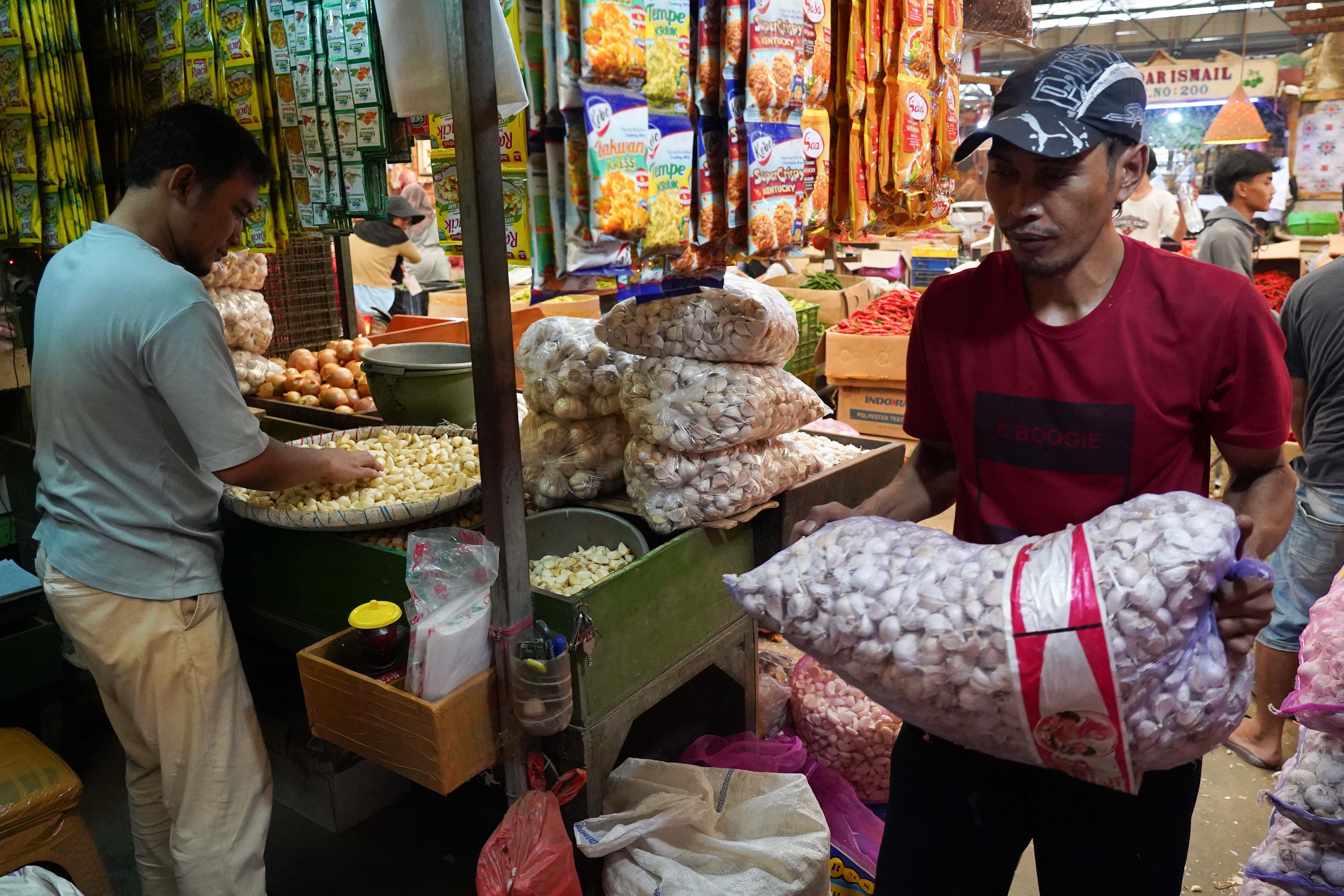 Pedagang membawa bawang putih impor yang dijual di Pasar Induk Kramat Jati, Jakarta, Selasa (14/7/2026). Berdasarkan pemantauan Indeks Perkembangan Harga (IPH), rata-rata harga bawang putih secara nasional kini mencapai Rp 42.611 per kilogram atau sudah berada jauh di atas Harga Acuan Penjualan (HAP) konsumen. Kenaikan ini disebabkan oleh melemahnya nilai tukar rupiah terhadap dolar Amerika Serikat (AS) dan meningkatnya biaya logistik internasional.