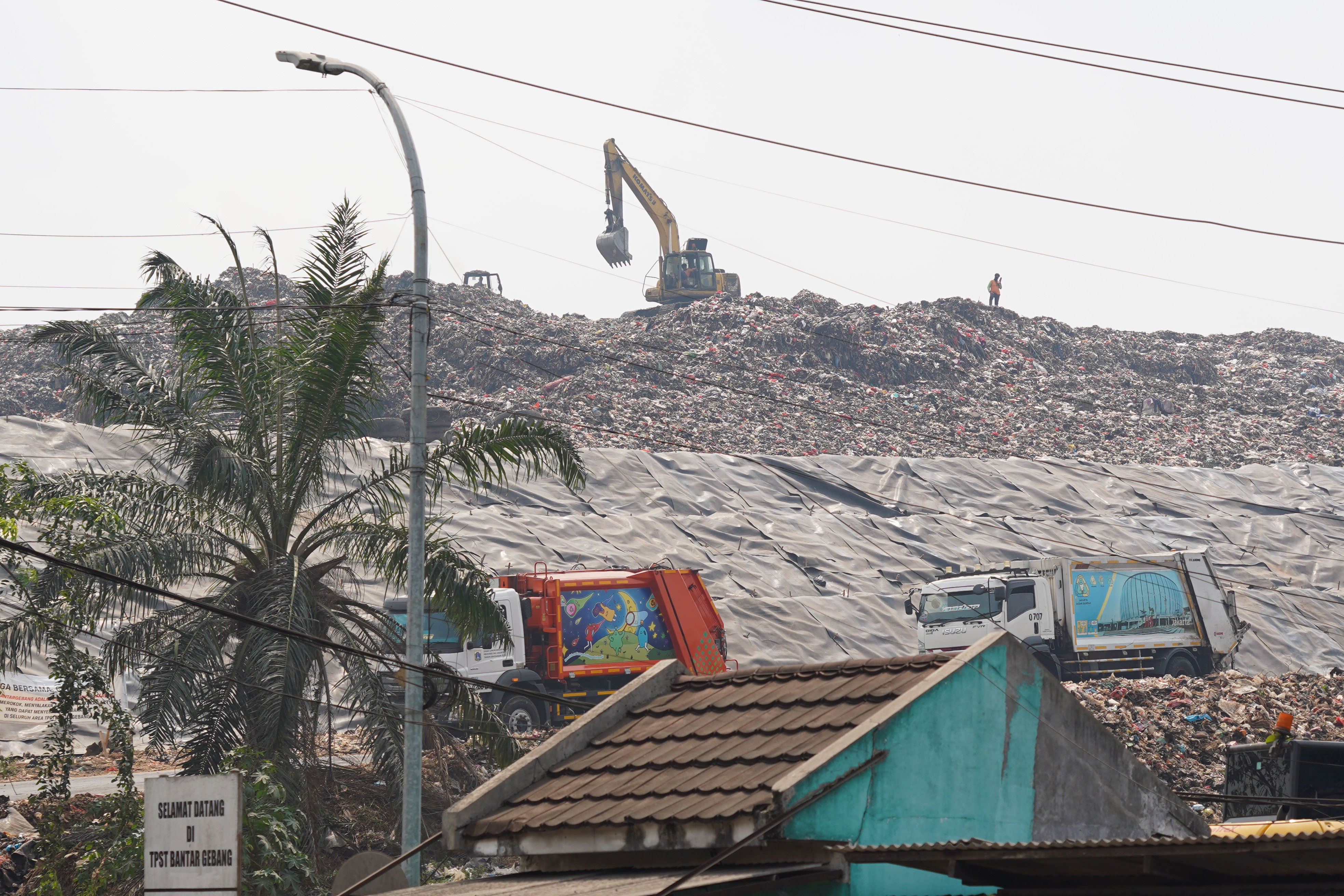 Alat berat eskavator memindahkan sampah di dekat tumpukan sampah yang telah ditutup geomembran di Tempat Pembuangan Sampah Terpadu (TPST) Bantargebang, Kota Bekasi, Jawa Barat, Selasa (4/8/2026). Pemasangan plastik kedap air tersebut merupakan transisi sistem pengolahan sampah dari praktik open dumping menuju controlled landfill yang ditargetkan sepenuhnya diterapkan pada 2029 untuk melindungi area timbunan dan mengurangi cemaran air lindi ke lingkungan.