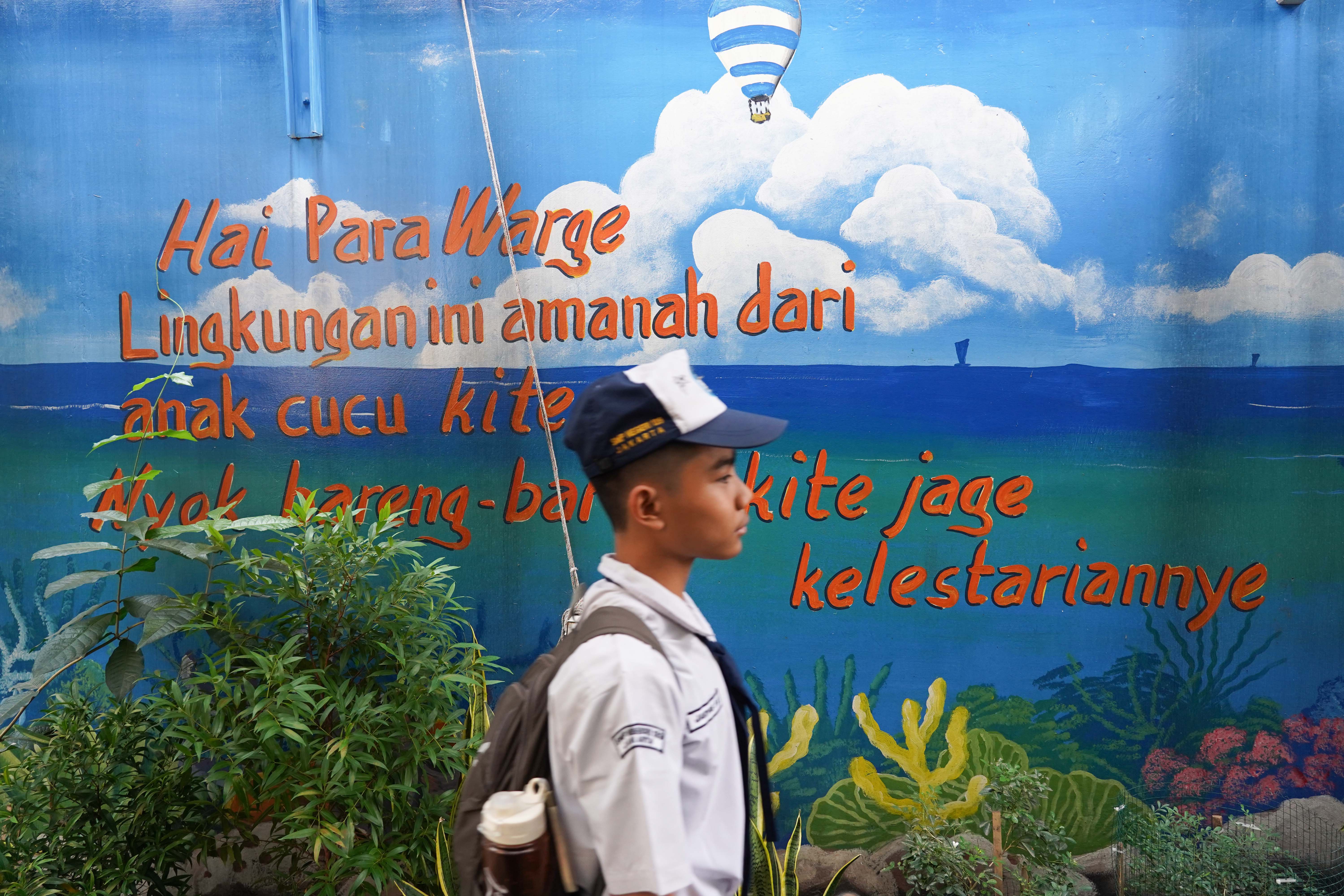 Pelajar berjalan dekat tulisan ajakan untuk menjaga lingkungan di kawasan Jalan Nusa Indah IV Gang 8, RT.08/RW.04, Malaka Jaya, Duren Sawit, Jakarta Timur. 