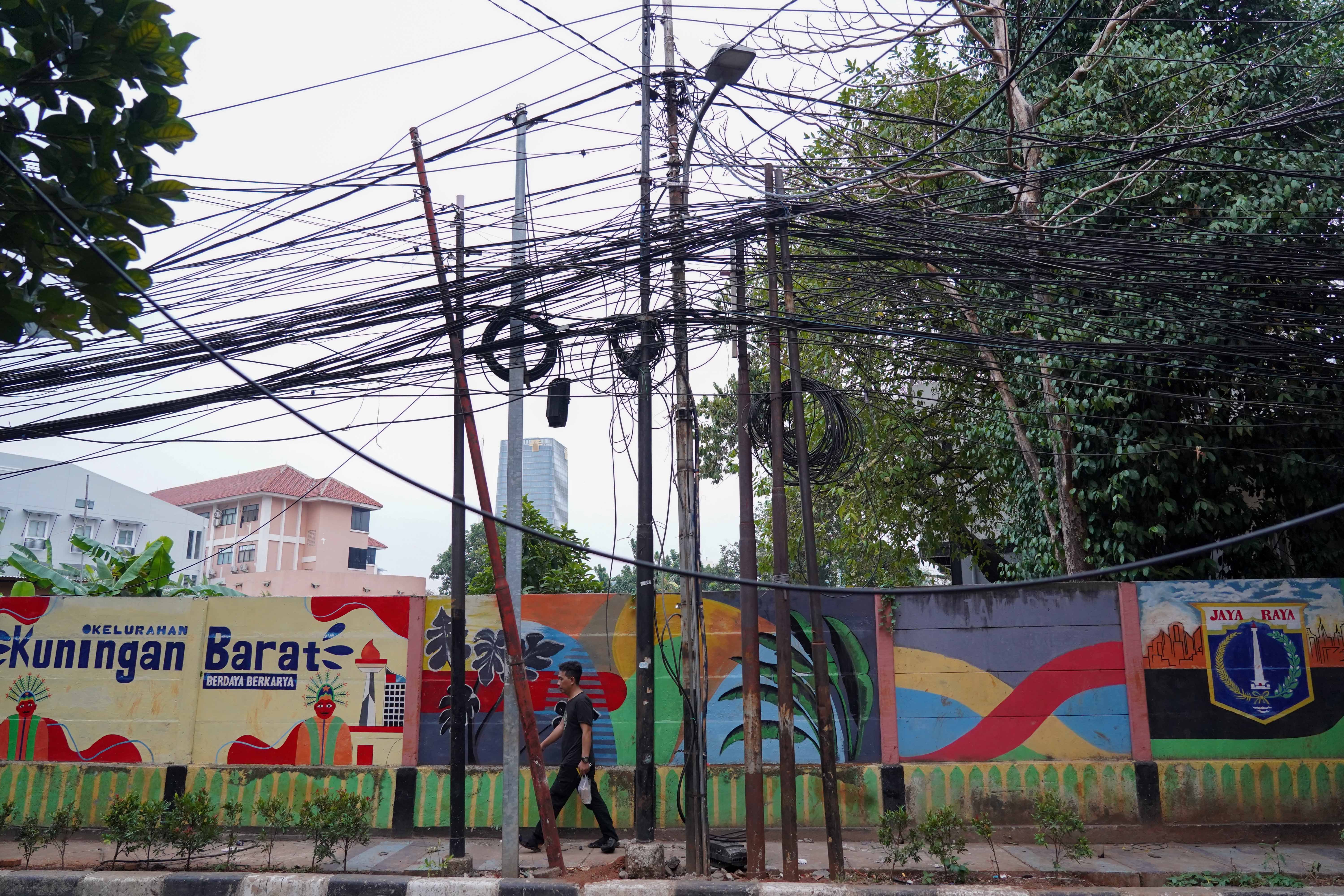 Warga berjalan di dekat kabel yang semrawut di kawasan Jalan Kuningan Barat Raya, Mampang Prapatan, Jakarta Selatan, Rabu (30/9/2026). Pemerintah Provinsi DKI Jakarta menargetkan seluruh kabel udara di Ibu Kota dapat diturunkan ke bawah tanah dalam lima tahun ke depan sebagai upaya memperbaiki wajah kota agar lebih rapi, aman dan nyaman bagi masyarakat.