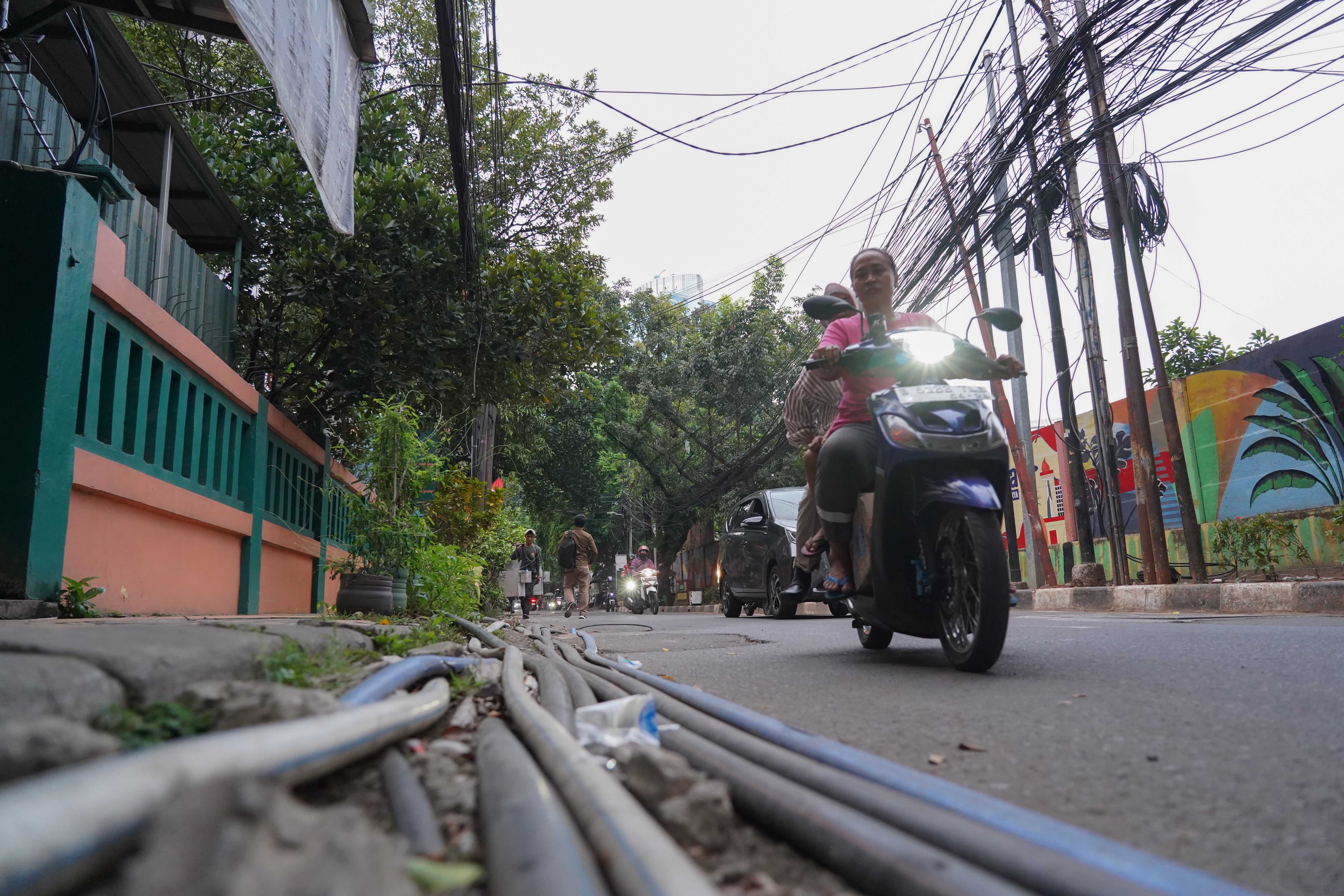 Pengendara sepeda motor melintas di dekat kabel yang semrawut di kawasan Jalan Kuningan Barat Raya, Mampang Prapatan, Jakarta Selatan, Rabu (30/9/2026). Pemerintah Provinsi DKI Jakarta menargetkan seluruh kabel udara di Ibu Kota dapat diturunkan ke bawah tanah dalam lima tahun ke depan sebagai upaya memperbaiki wajah kota agar lebih rapi, aman dan nyaman bagi masyarakat.
