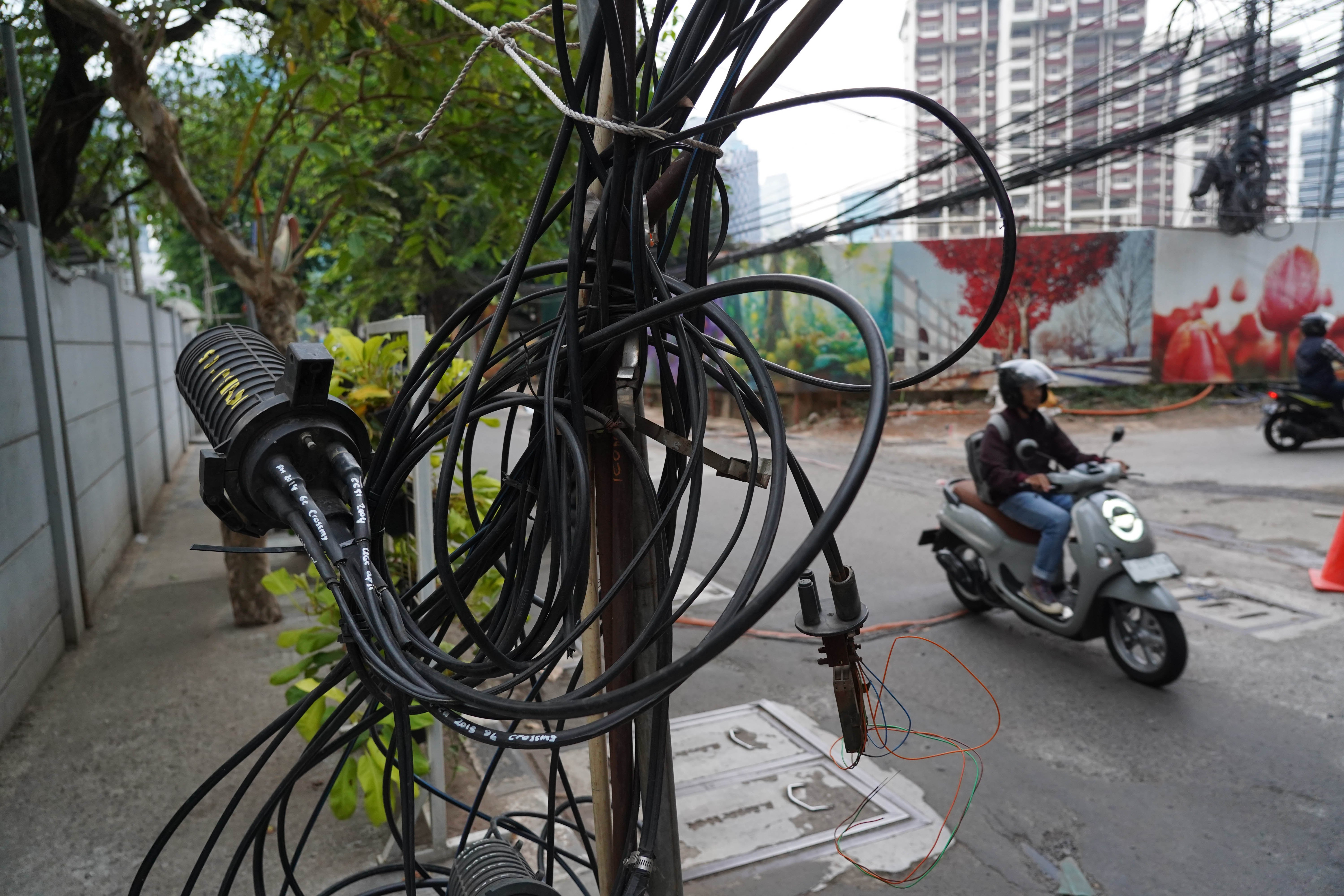 Pengendara sepeda motor melintas di dekat kabel yang semrawut di kawasan Jalan Kuningan Barat Raya, Mampang Prapatan, Jakarta Selatan, Rabu (30/9/2026). Pemerintah Provinsi DKI Jakarta menargetkan seluruh kabel udara di Ibu Kota dapat diturunkan ke bawah tanah dalam lima tahun ke depan sebagai upaya memperbaiki wajah kota agar lebih rapi, aman dan nyaman bagi masyarakat.
