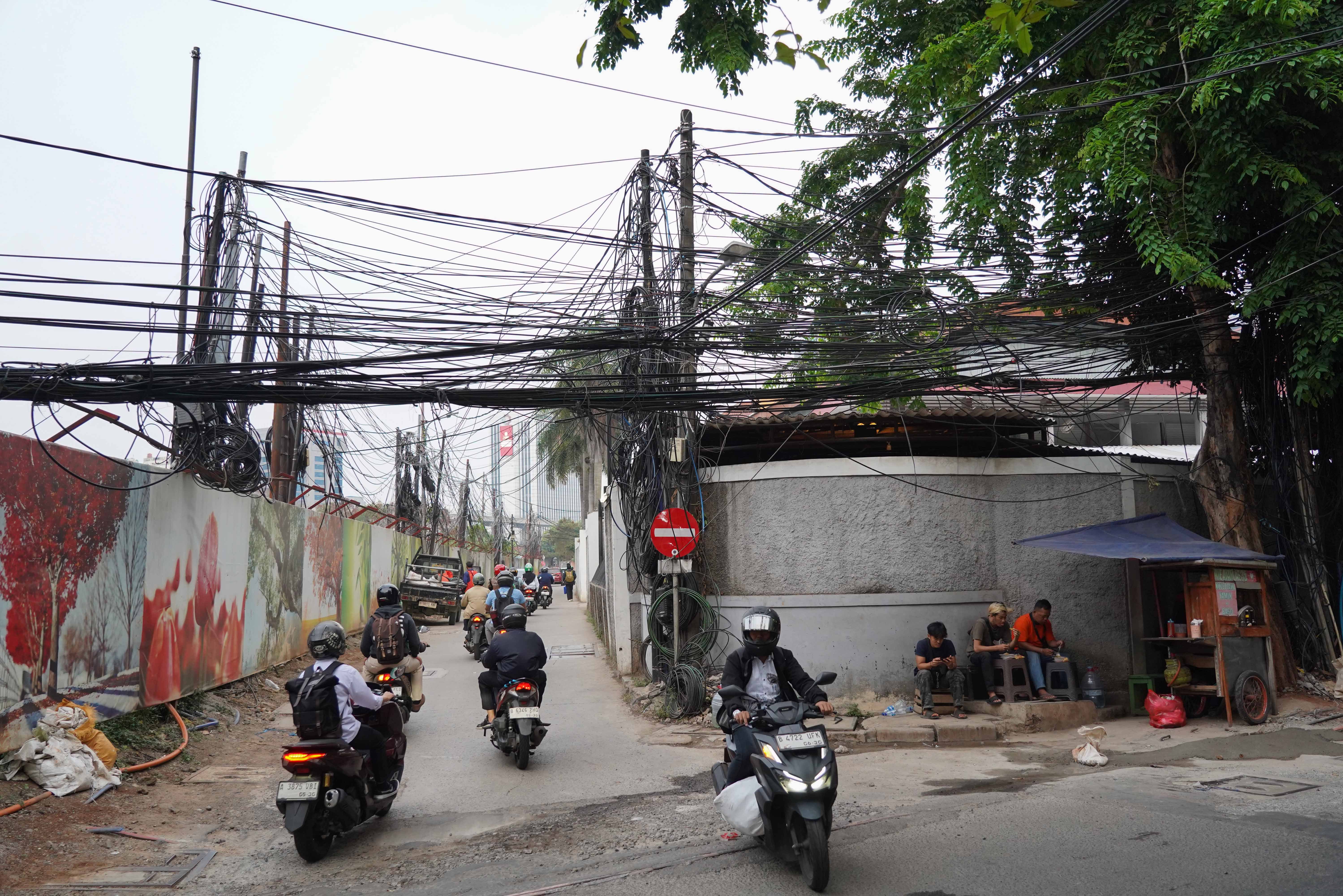 Pengendara sepeda motor melintas di dekat kabel yang semrawut di kawasan Jalan Kuningan Barat Raya, Mampang Prapatan, Jakarta Selatan, Rabu (30/9/2026). Pemerintah Provinsi DKI Jakarta menargetkan seluruh kabel udara di Ibu Kota dapat diturunkan ke bawah tanah dalam lima tahun ke depan sebagai upaya memperbaiki wajah kota agar lebih rapi, aman dan nyaman bagi masyarakat.