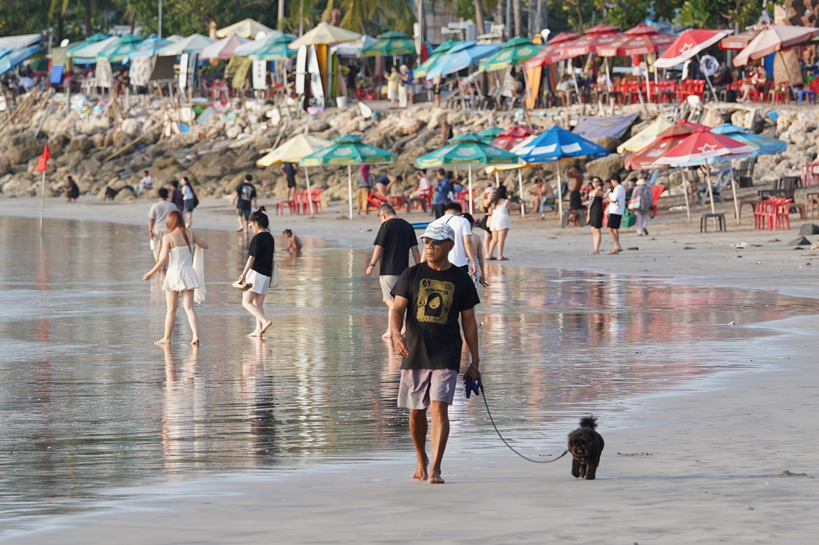 Wisatawan berjalan dengan hewan peliharaannya saat berkunjung ke Pantai Kuta di Kabupaten Badung, Bali, Kamis (8/10/2026). Pantai yang memiliki luas sekitar 2,5 kilometer ini dikenal sebagai salah satu destinasi wisata di Pulau Dewata yang menawarkan pesona keindahan mulai dari hamparan pasir putih, ombak yang ideal untuk berselancar hingga pemandangan sunset yang memukau.