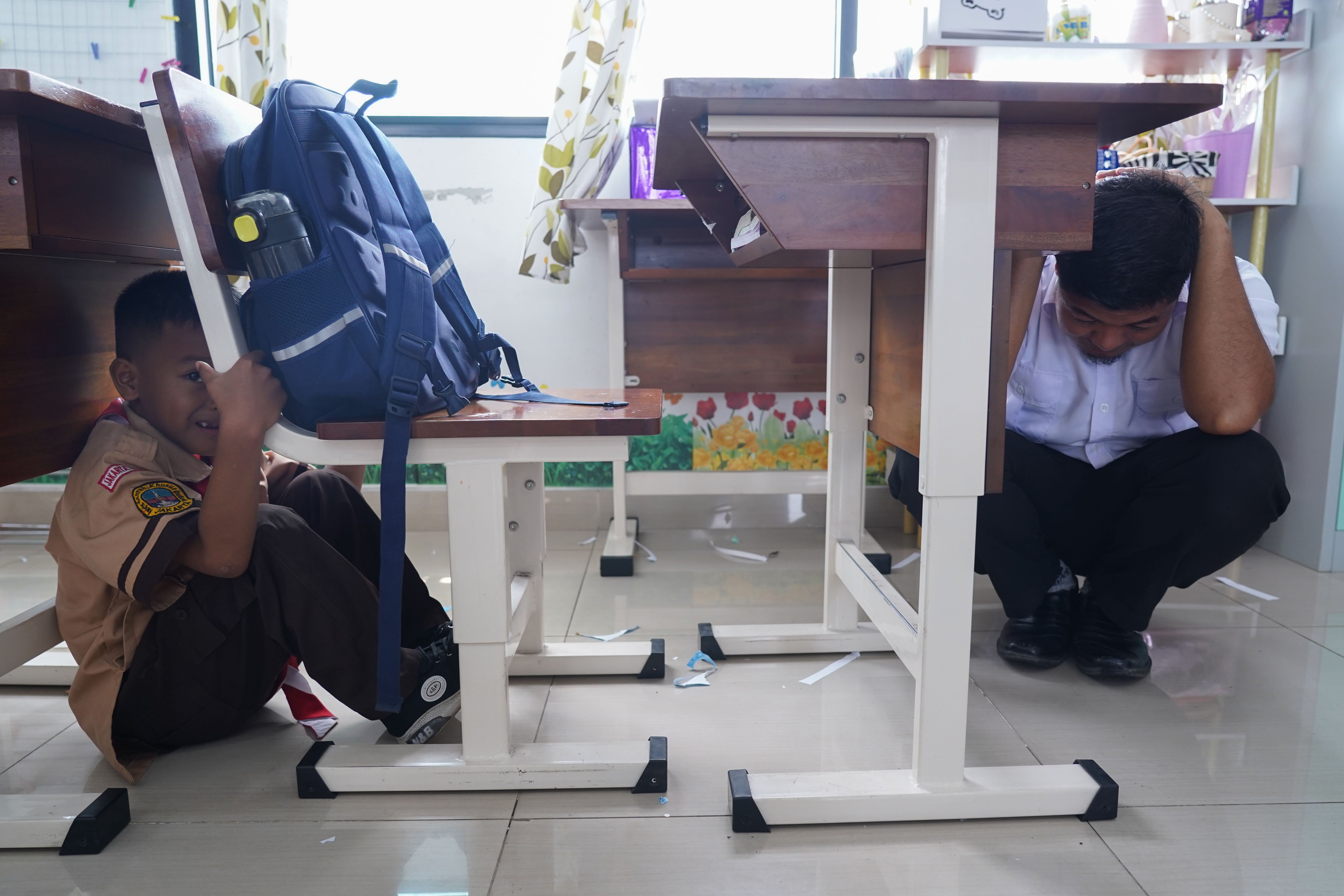 Guru dan siswa berlindung di bawah meja saat mengikuti simulasi gempa bumi di SDN Pejaten Timur 11, Jakarta, Rabu (21/10/26). Pemerintah Provinsi DKI Jakarta menggelar simulasi gempa bumi serentak pada 21 Oktober 2026 di gedung perkantoran pemerintah, kantor kecamatan dan kelurahan hingga sekolah dalam rangka meningkatkan kesiapsiagaan menghadapi potensi bencana gempa bumi.