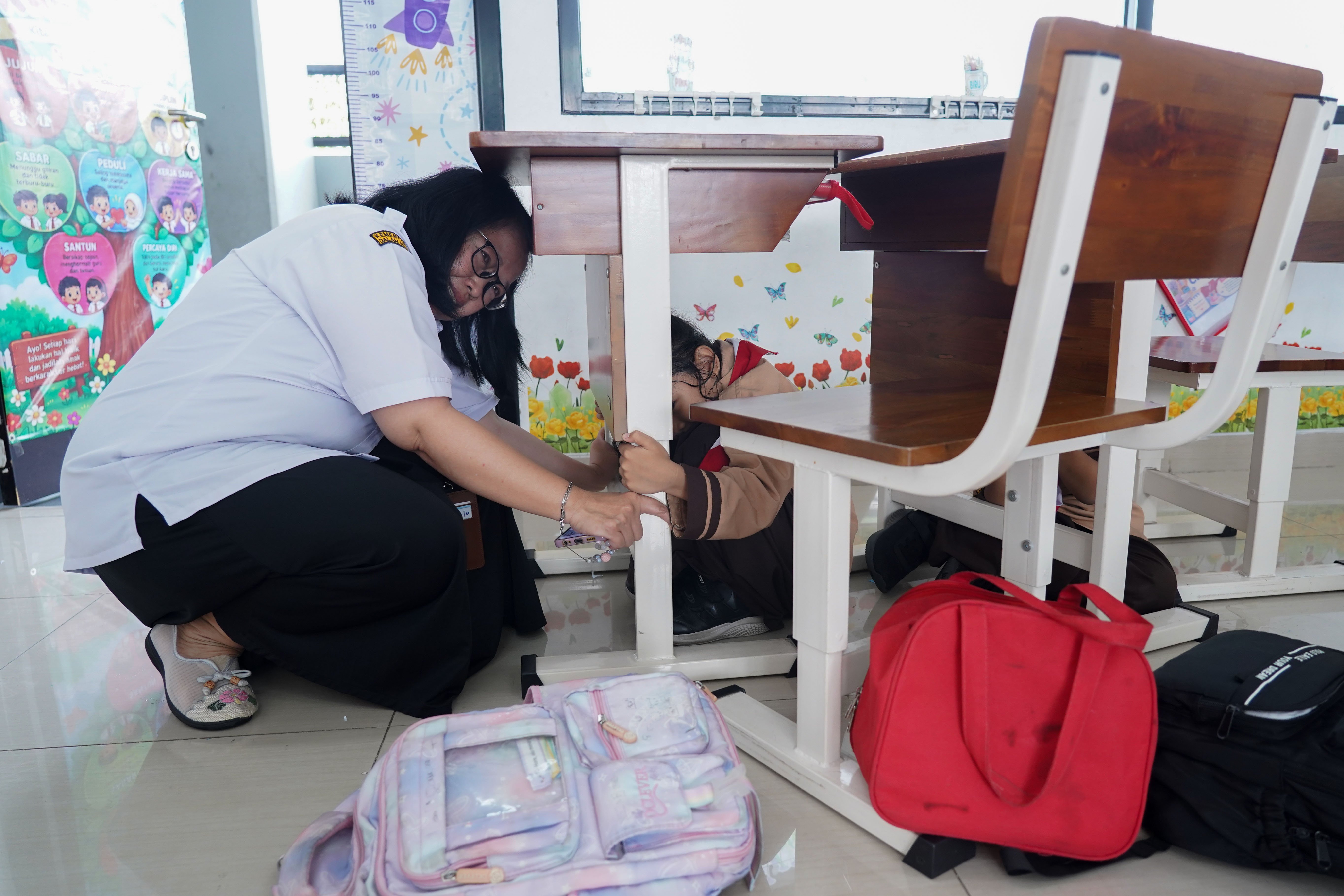 Guru dan siswa berlindung di bawah meja saat mengikuti simulasi gempa bumi di SDN Pejaten Timur 11, Jakarta, Rabu (21/10/26). Pemerintah Provinsi DKI Jakarta menggelar simulasi gempa bumi serentak pada 21 Oktober 2026 di gedung perkantoran pemerintah, kantor kecamatan dan kelurahan hingga sekolah dalam rangka meningkatkan kesiapsiagaan menghadapi potensi bencana gempa bumi.