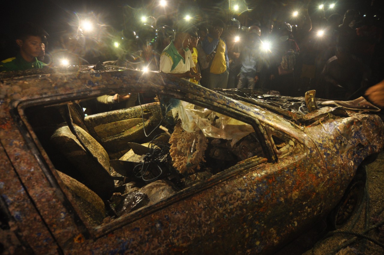 Sejumlah warga mengamati bangkai kendaraan yang diangkat dari dasar laut di Pantai Mamboro, Palu, Sulawesi Tengah, Selasa (19/11/2019). Sebuah bangkai mobil jenis sedan yang diduga terseret gelombang tsunami pada peristiwa gempa 28 September 2018 ditemukan oleh nelayan saat melaut dan pemiliknya belum diketahui. Foto Pilihan Pekan Ketiga November 2019