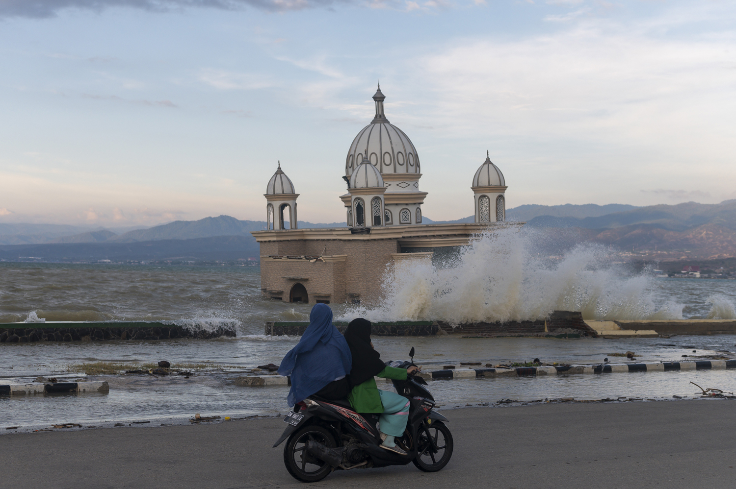 Pengendara sepeda motor melintas di dekat masjid yang posisinya saat ini terendam air laut pasca terkena tsunami tahun 2018, di Pantai Kampung Lere, Teluk Palu, Sulawesi Tengah, Rabu (27/11/2019). Badan Meteorologi, Klimatologi dan Geofisika (BMKG) mengeluarkan peringatan dini gelombang tinggi di sejumlah wilayah di Indonesia yang berbahaya untuk pelayaran bagi kapal tertentu. Foto Pilihan Pekan Keempat November 2019