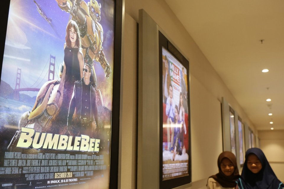 Dua orang pengunjung Cinema XXI Jatinegara melintas di depan poster film Bumblebee, Matraman, Jakarta Timur (26/12).