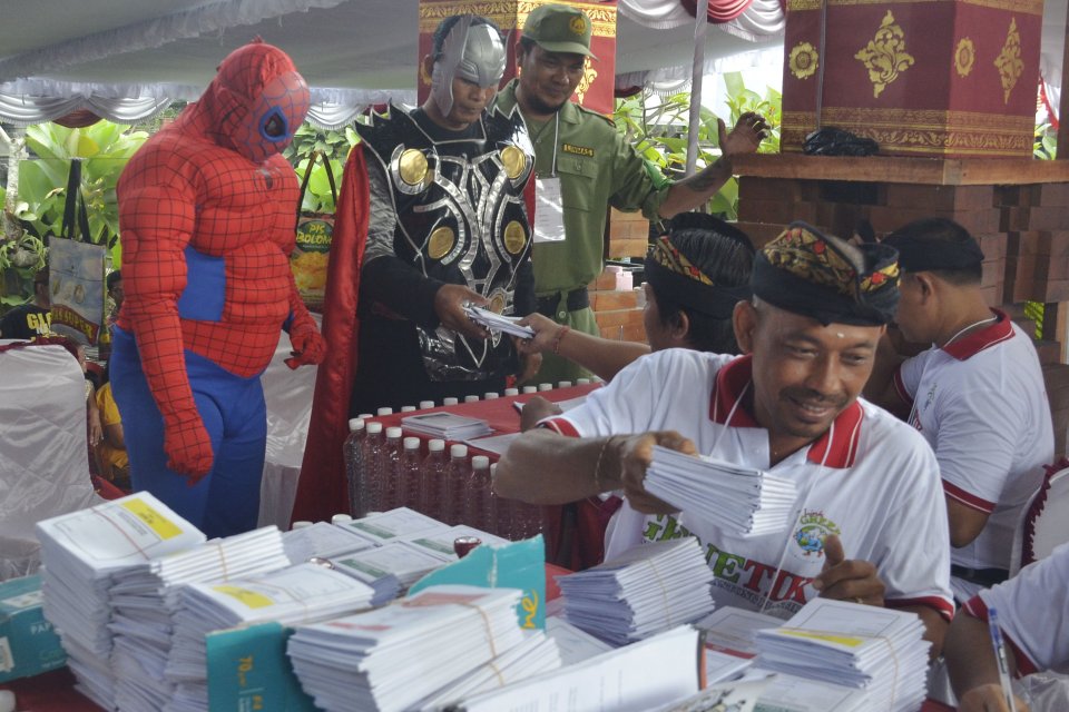 Petugas Kelompok Penyelenggara Pemungutan Suara (KPPS) menyerahkan surat suara kepada warga yang mengenakan kostum \"superhero\" atau pahlawan super karakter Spiderman dan Thor saat menggunakan hak suaranya dalam Pemilu 2019 di TPS 10 Banjar Ubung Sem
