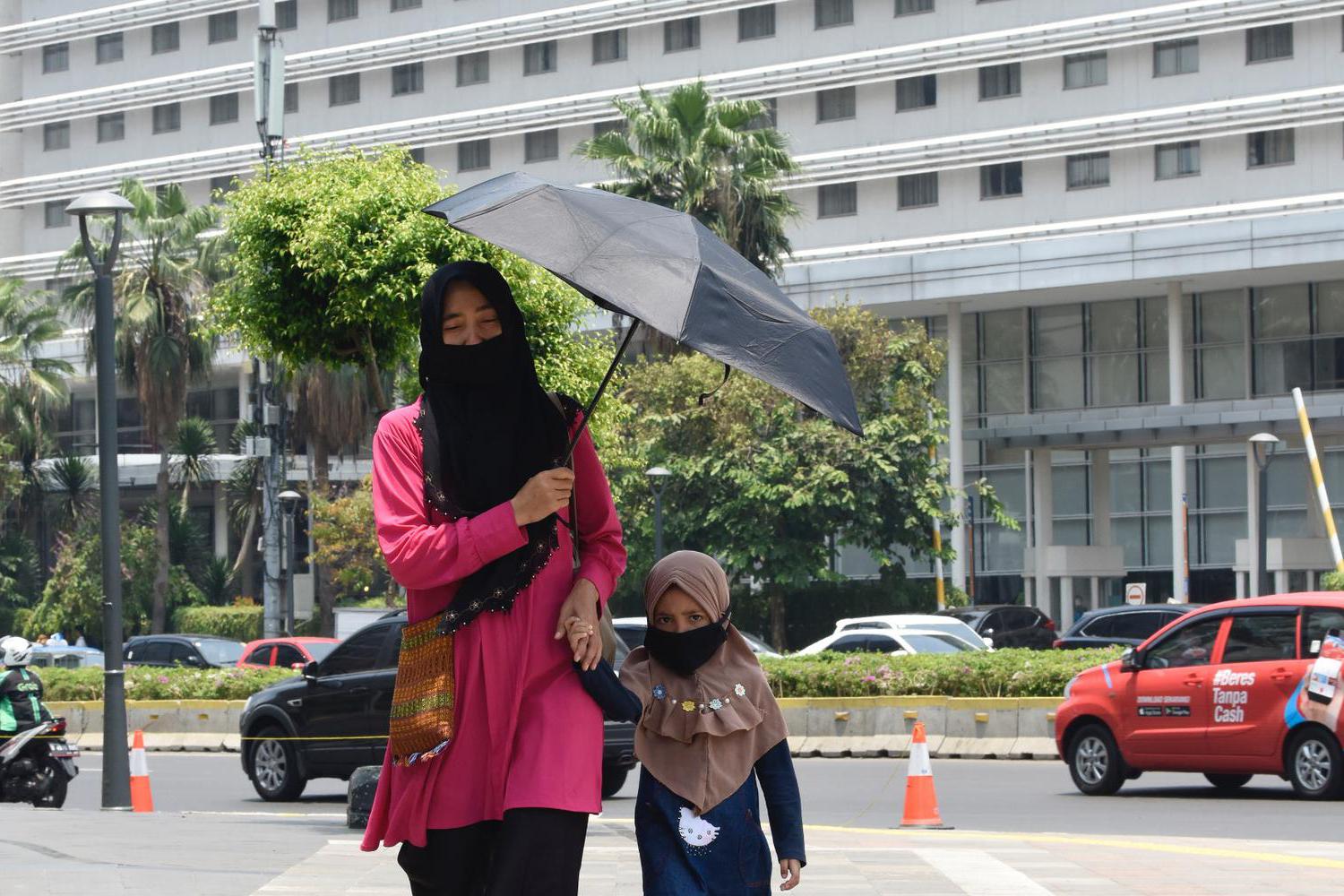 Seorang bersama anaknya menggunakan payung untuk menghindari sengatan matahari ketika berjalan di sekitar Bunderan HI, Jakarta, Rabu (23/10/2019).. BMKG menghimbau kepada masyarakat agar mewaspadai kondisi cuaca ekstrim pada siang hari terutama di Pulau J