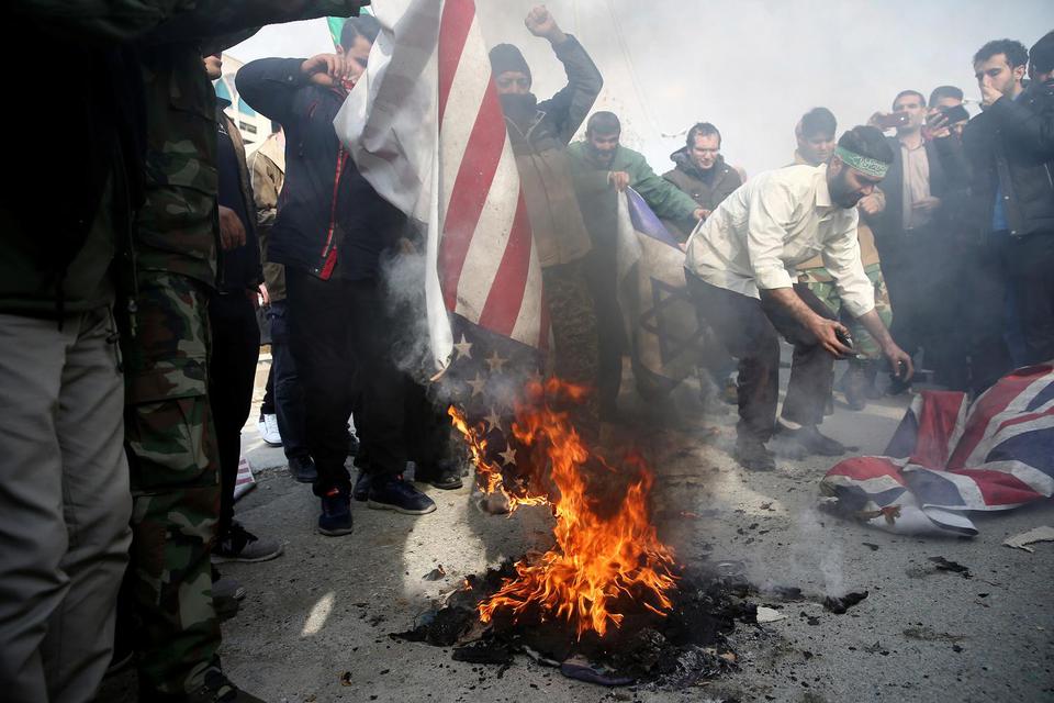 Demonstran membakar bendera Amerika Serikat, Israel dan Inggris saat aksi protes menentang pembunuhan Mayor Jenderal Iran Qassem Soleimani, kepala pasukan elit Quds, dan komandan milisi Irak Abu Mahdi al-Muhandis, yang tewas saat serangan udara di bandara