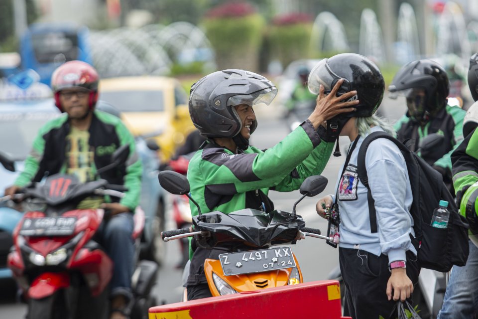 Pengemudi ojek online memasang helm kepada penumpang, di Kawasan Sudirman-Thamrin, Jakarta Pusat, (17/2/2020). Belum sampai satu tahun diterapkan tarif baru ojek online, kini tarifnya akan disesuaikan kembali. Kenaikan tarif tersebut rencananya akan dibe