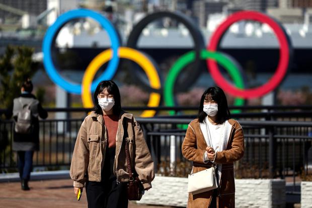 Warga dengan masker pelindung akibat mewabahnya virus korona, berada di depan cincin Olimpiade Raksasa di area tepi laut Taman Marina Odaiba, Tokyo, Jepang, Kamis (27/2/2020).