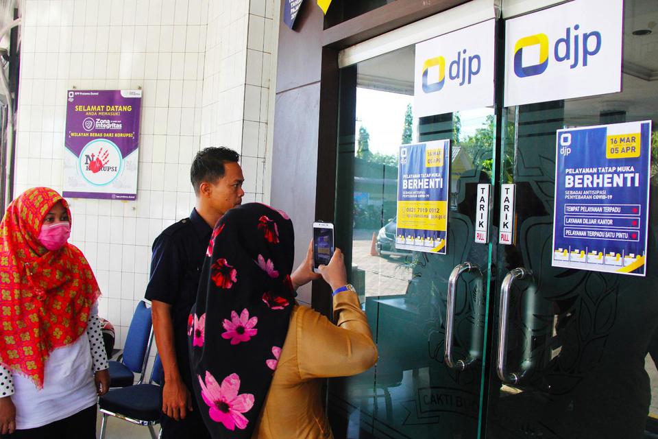 Seorang pengunjung mengambil gambar tanda pemberitahuan penghentian pelayanan pajak langsung sebagai antisipasi penyebaran COVID-19 di depan pintu masuk Kantor Pelayanan Pajak (KPP) Pratama Dumai di Dumai, Riau, Senin (16/3/2020).
