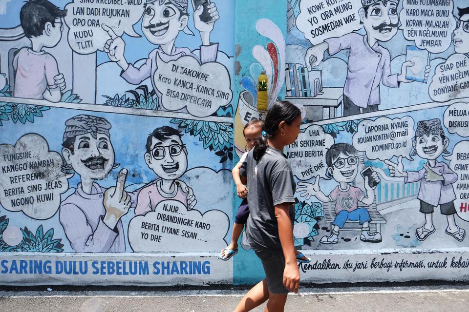 Warga melewati mural (lukisan dinding) komik antihoaks di Kampung Hepi, Joho, Manahan, Solo, Jawa Tengah, Selasa (7/4/2020). 