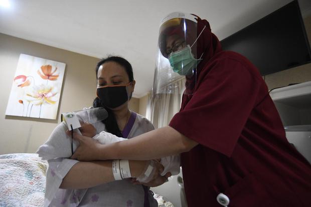 Perawat mengantarkan bayi yang memakai pelindung muka atau 'face shield' di RS Ibu dan Anak Asih, Jakarta, Jumat (17/4/2020). RSIA Asih memberikan perlindungan dini berupa pelindung muka atau 'face shield' kepada bayi baru lahir, bayi atau anak yang m
