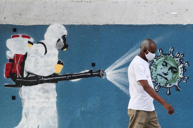 Sergio Moraes Seorang pria berjalan di sebelah grafiti yang menggambarkan petugas kebersihan memakai alat pelindung diri menyemprotkan virus berwajah Presiden Brasil Jair Bolsonaro ditengah wabah penyakit virus corona (COVID-19), di Rio de Janeiro, 