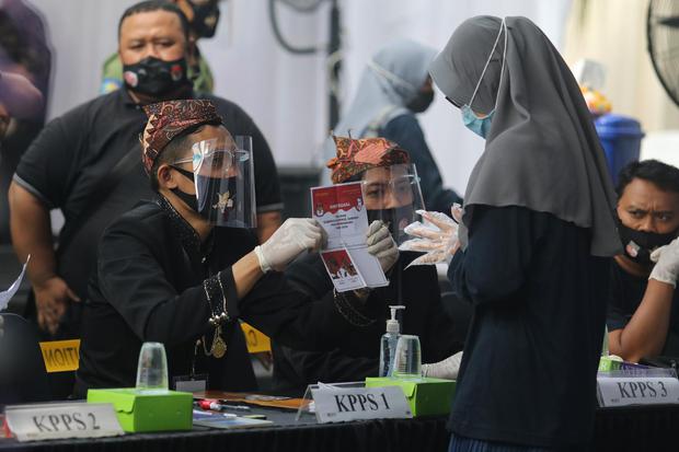 Petugas menggunakan masker, pelindung wajah, dan kaos tangan memberikan surat suara kepada calon pemilih saat simulasi nasional pemungutan suara Pilkada serentak di Kediri, Jawa Timur, Sabtu (31/10/2020). Simulasi nasional yang dihadiri ketua KPU Arief Bu