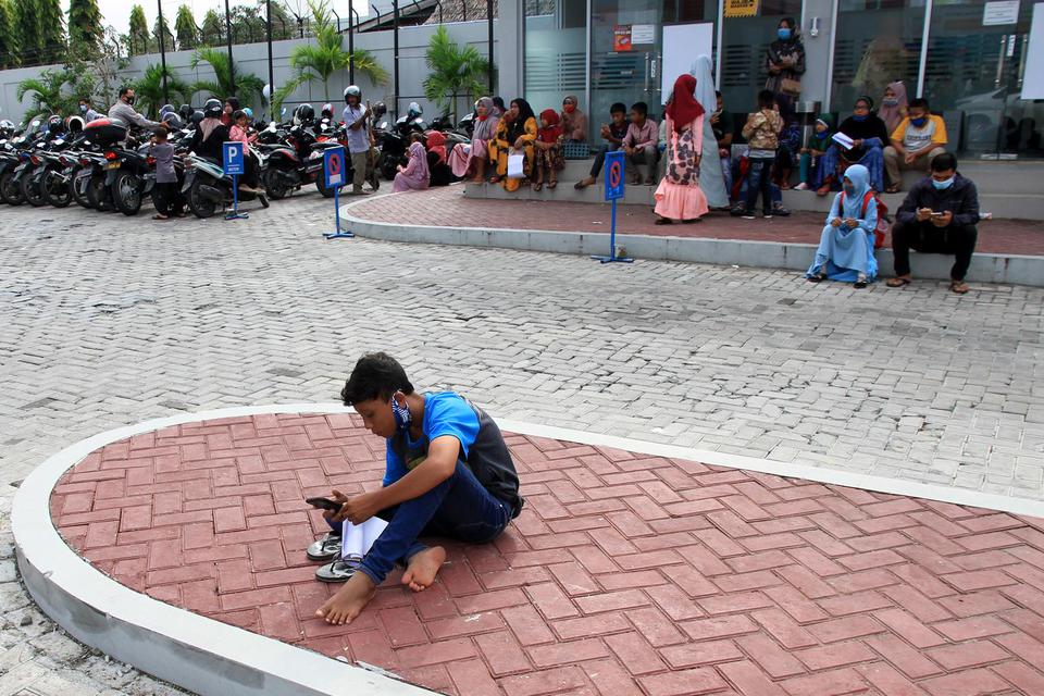 Sejumlah anak ditemani orang tuanya menunggu antrian proses pencairan Bantuan Langsung Tunai (BLT) Program Indonesia Pintar (PIP) di halaman Bank Rakyat Indonesia (BRI) cabang Meulaboh, Aceh Barat, Aceh, Selasa (2/2/2021).