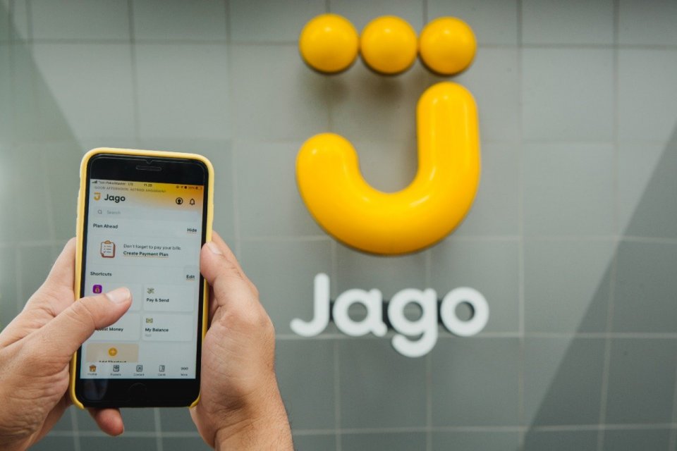 Seorang nasabah membuka aplikasi Bank Jago di depan logo bank digital tersebut