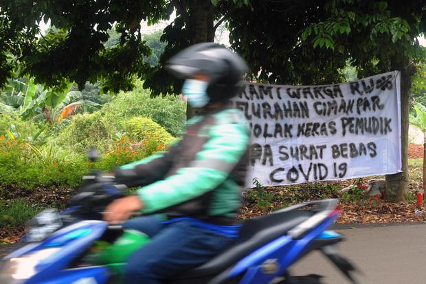 Pengemudi ojek daring melintas di dekat spanduk penolakan warga terhadap pemudik di Kelurahan Cimahpar, Kota Bogor, Jawa Barat, Selasa (18/5/2021).