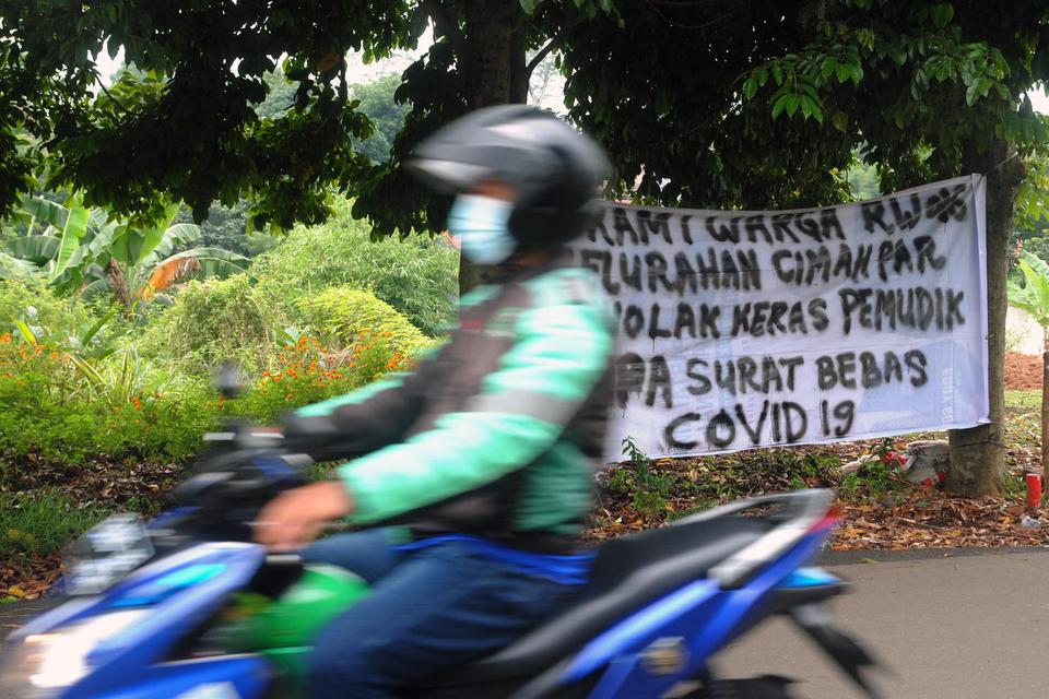 Pengemudi ojek daring melintas di dekat spanduk penolakan warga terhadap pemudik di Kelurahan Cimahpar, Kota Bogor, Jawa Barat, Selasa (18/5/2021).