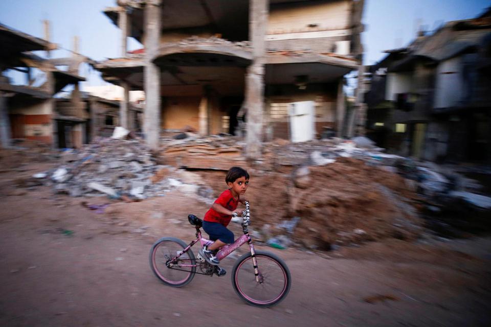 Seorang anak lelaki mengayuh sepedanya di dekat reruntuhan sebuah rumah yang hancur akibat serangan udara Israel saat perseteruan antara Israel-Hamas, di Jalur Gaza, Minggu (23/5/2021).