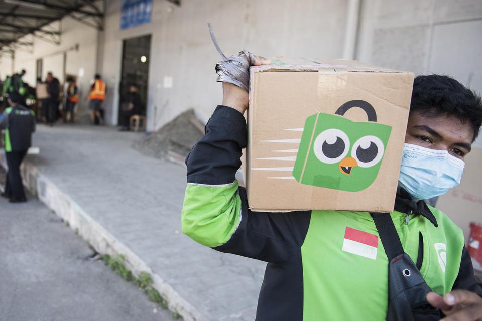 Pengemudi daring Gojek membawa kemasan paket dari Tokopedia di Titipaja Warehouse, Jakarta, Jumat (28/5/2021). Kementerian Koperasi dan UKM menyatakan kolaborasi bisnis yang dilakukan oleh dua startup raksasa Gojek dan Tokopedia, melalui pembentukan GoTo 