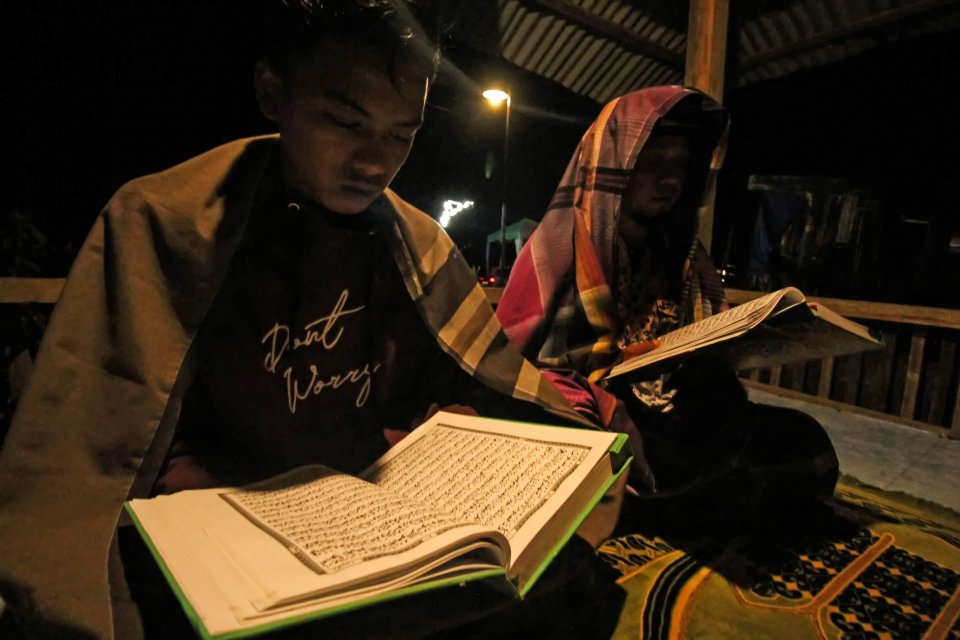Sejumlah warga membaca Al-quran dengan penerangan lampu yang tersalur dengan jaringan listrik melalui program listrik masuk wilayah desa tertinggal di Dusun Jabal Antara, Aceh Utara. Surat Al Falaq menerangkan perlindungan Allah pada umat Islam dari berba