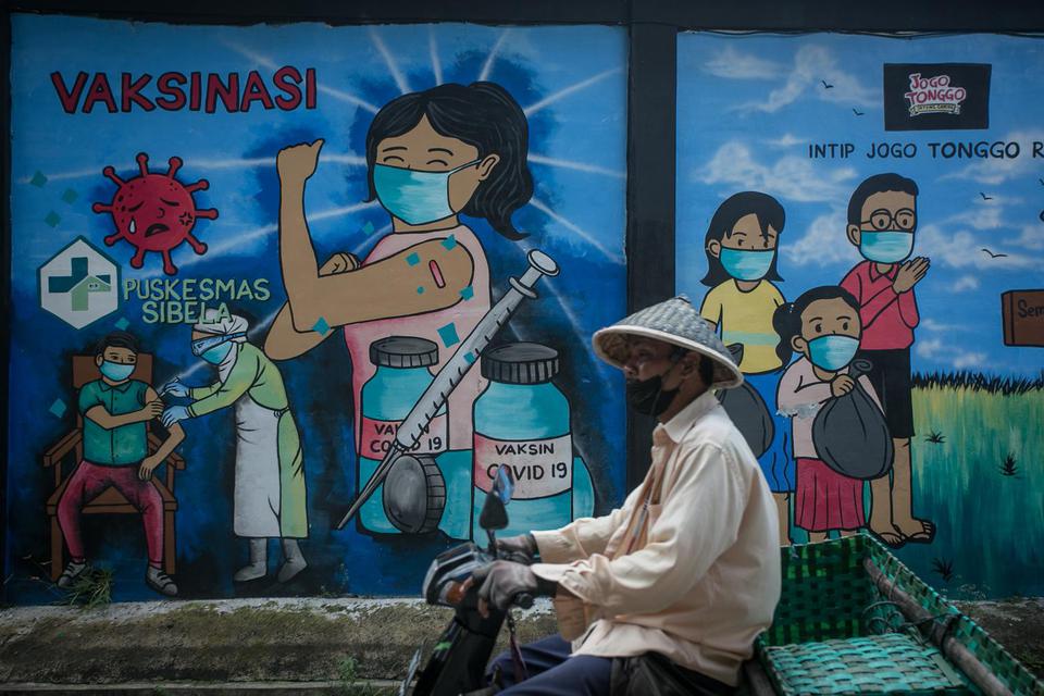 Warga melintas di depan mural bertema ajakan vaksinasi di Mojosongo, Solo, Jawa Tengah, Selasa (8/3/2022). 