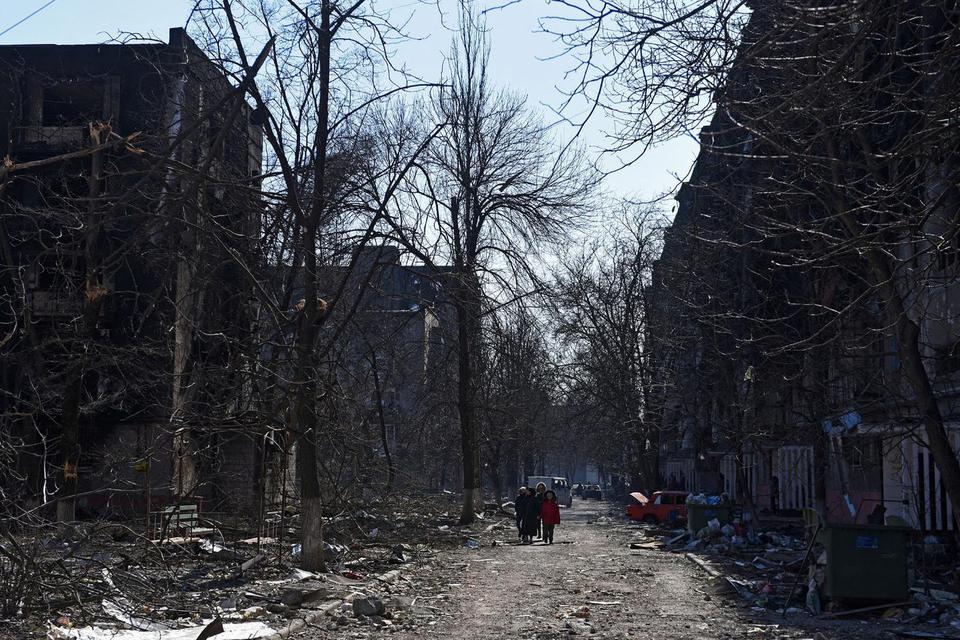 Stringer Warga setempat berjalan dekat gedung pemukiman yang hancur akibat konflik Ukraina-Rusia di kota pelabuhan terkepung Mariupol, Ukraina, Jumat (18/3/2022).