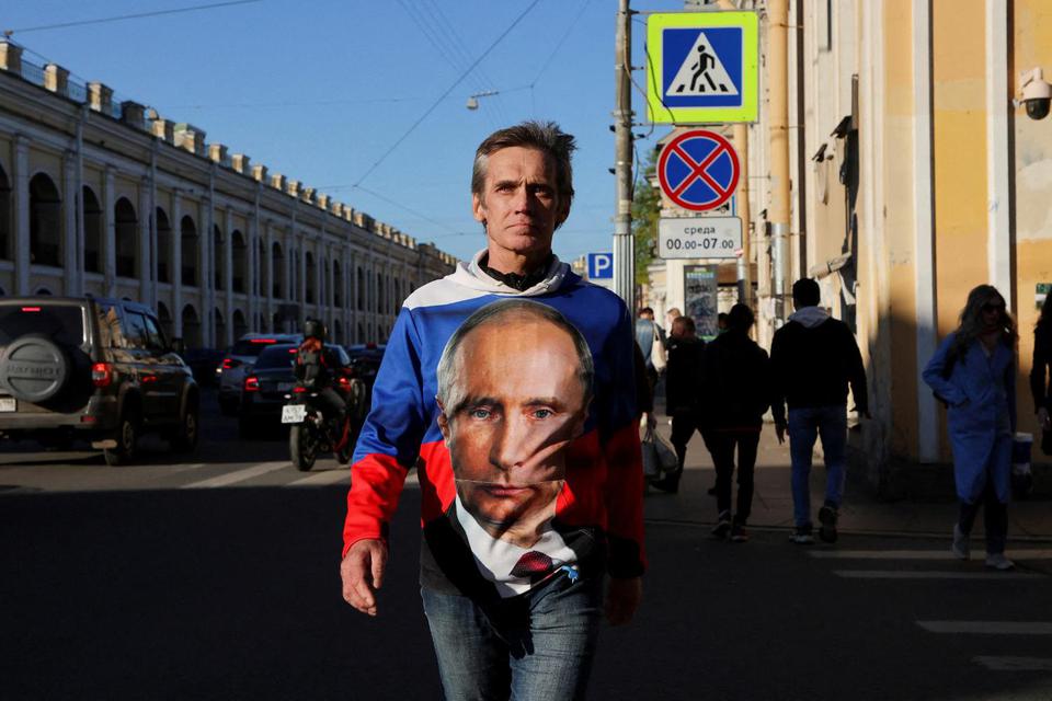 Seorang pria mengenakan kemeja yang dicetak dengan warna bendera nasional Rusia dan menggambarkan Presiden Rusia Vladimir Putin, melintasi jalan di Saint Petersburg, Rusia, Sabtu (21/5/2022).