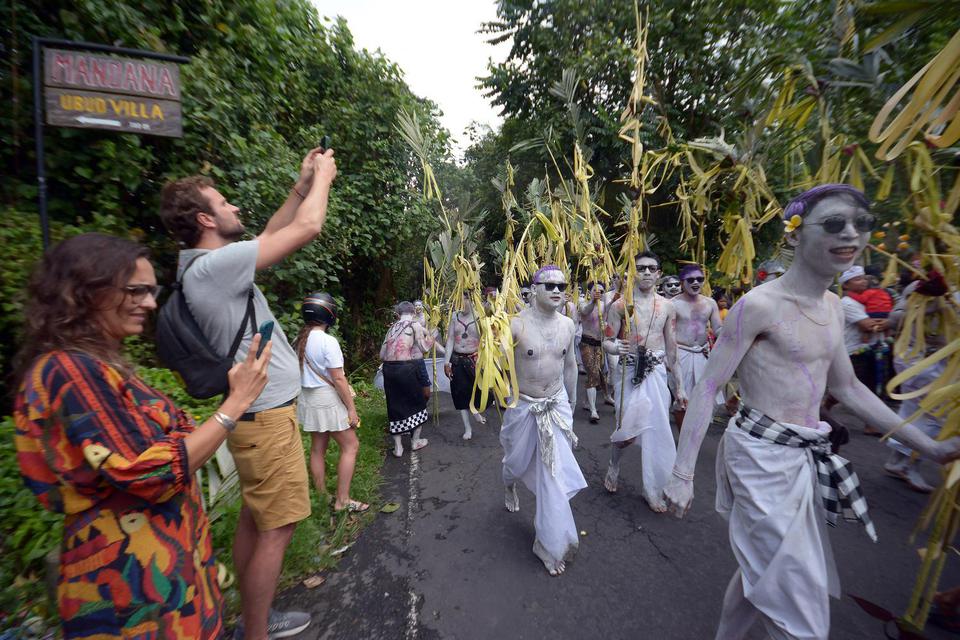 Wisatawan menyaksikan warga yang berhias warna-warni berjalan berkeliling desa dengan membawa berbagai sarana upacara saat tradisi Ngerebeg di Desa Tegallalang, Gianyar, Bali, Rabu (13/7/2022). 