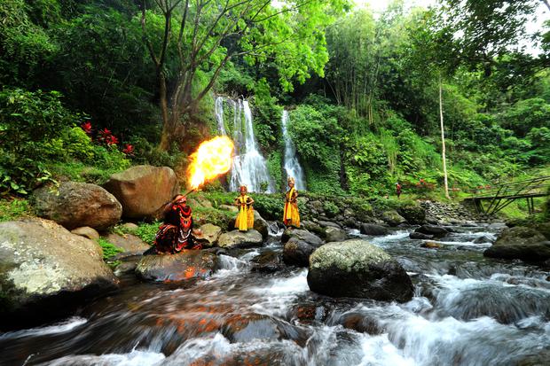 Seniman jaranan buto menyemburkan api dengan latar belakang air terjun Jagir di Banyuwangi, Jawa Timur, Kamis (22/09/2022). Sejumlah seniman tari bersama pengelola wisata mengkolaborasikan unsur seni daerah setempat sebagai pariwisata yang berbasis budaya