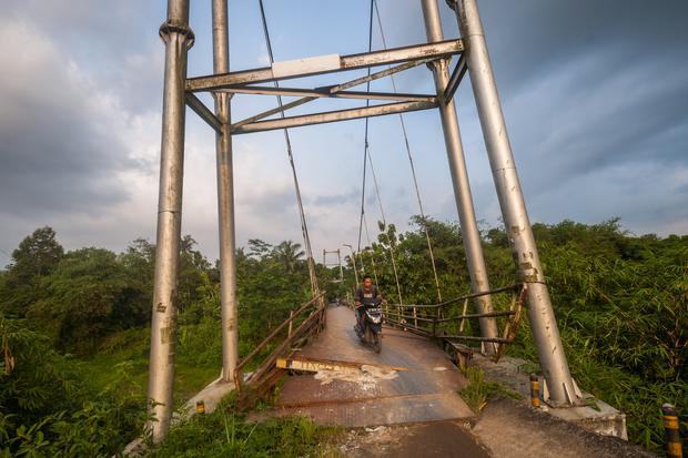 Pengendara sepeda motor melintasi jembatan gantung yang rusak di Rangkasbitung, Lebak, Banten, Minggu (25/9/2022). Jembatan tersebut konstruksi telah miring dan sebagian besinya mengalami kerusakan sehingga membahayakan bagi yang melintas.