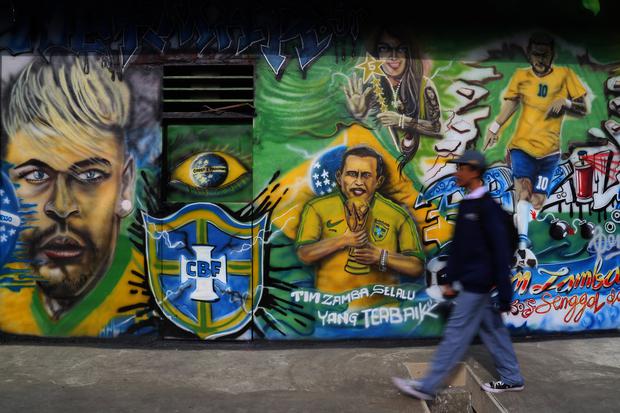 Warga melintas di depan mural Timnas Brazil di Komlpeks Tanah Tinggi Baru, Kota Ternate, Maluku Utara, Senin (28/11/2022). Warga setempat sengaja menggambar mural Timnas Brazil di rumahnya untuk menyemarakkan Piala Dunia 2022 Qatar sekaligus menarik wisa