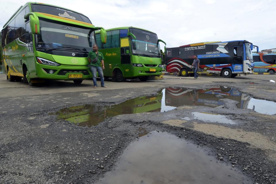 Sejumlah awak angkutan umum menunggu penumpang di dekat jalan yang rusak dan tergenang air di Terminal Rajabasa, Bandar Lampung, Lampung, Sabtu (1/4/2023). Tidak terawatnya infrastruktur dan rusaknya jalan di terminal tersebut menyebabkan aktivitas awak a