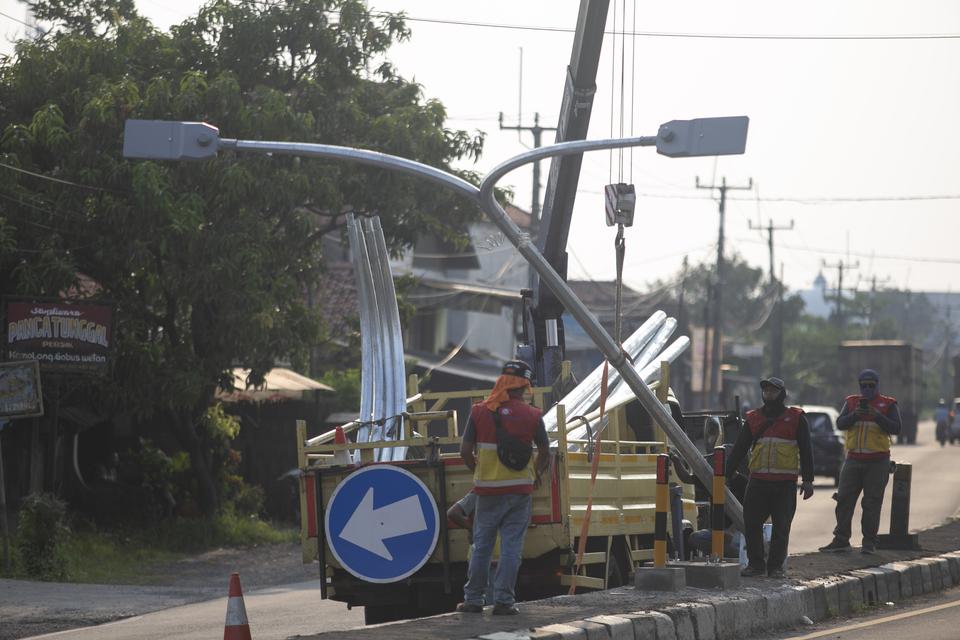 Pekerja menyelesaikan pemasangan lampu Penerangan Jalan Umum (PJU) di Jalur Pantura Losarang, Indramayu, Jawa Barat, Minggu (9/4/2023). Pemasangan lampu PJU di jalur pantura tersebut untuk meningkatkan kenyamanan para pemudik saat arus mudik mendatang.