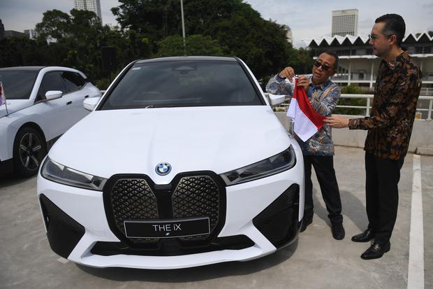 Sekretaris Kementerian Sekretariat Negara (Kemensetneg) Setya Utama (kiri) memasang bendera merah putih dibantu President Director of BMW Group Indonesia Ramesh Divyanathan (kanan) usai acara serah terima mobil resmi KTT ASEAN BMW iX di Jakarta, Kamis (13