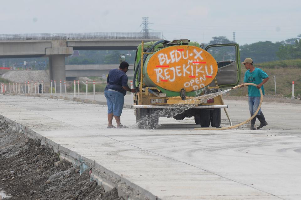 Pekerja menyemprotkan air pada jalan tol fungsional Solo-Yogyakarta di Banyudono, Boyolali, Jawa Tengah, Kamis (13/4/2023). Penyemprotan air itu dilakukan untuk membersihkan debu sisa-sisa pembangunan jalur tol Solo-Yogyakarta sebagai kesiapan sebagai jal