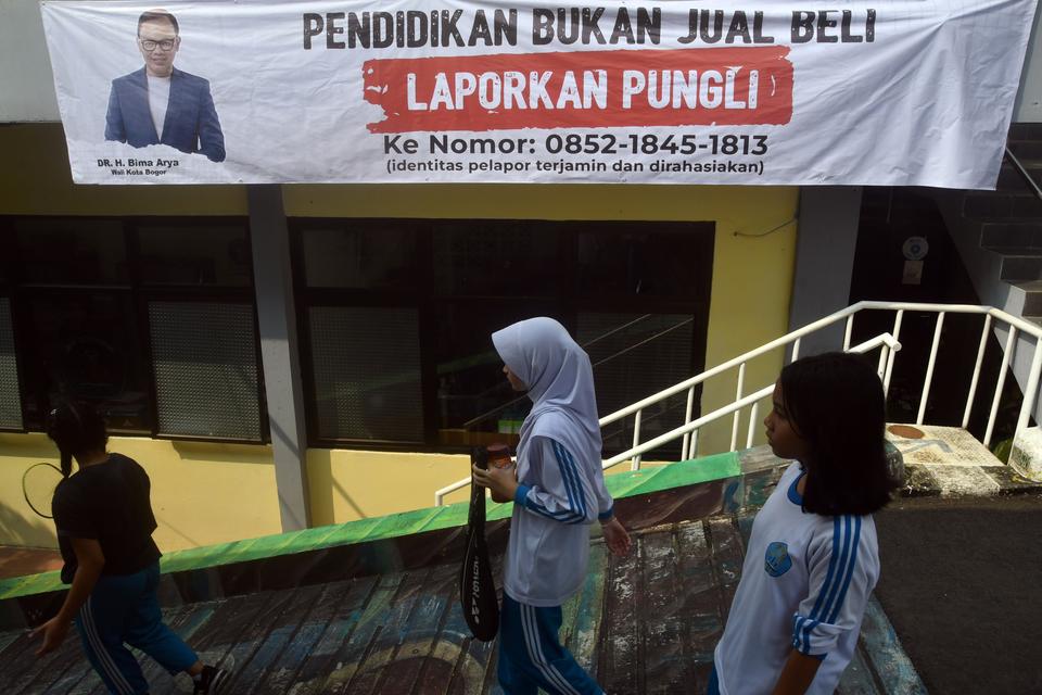 Siswa berjalan di samping spanduk sosialisasi masalah pungli di SMPN 8 Kota Bogor, Jawa Barat, Senin (7/8/2023). 