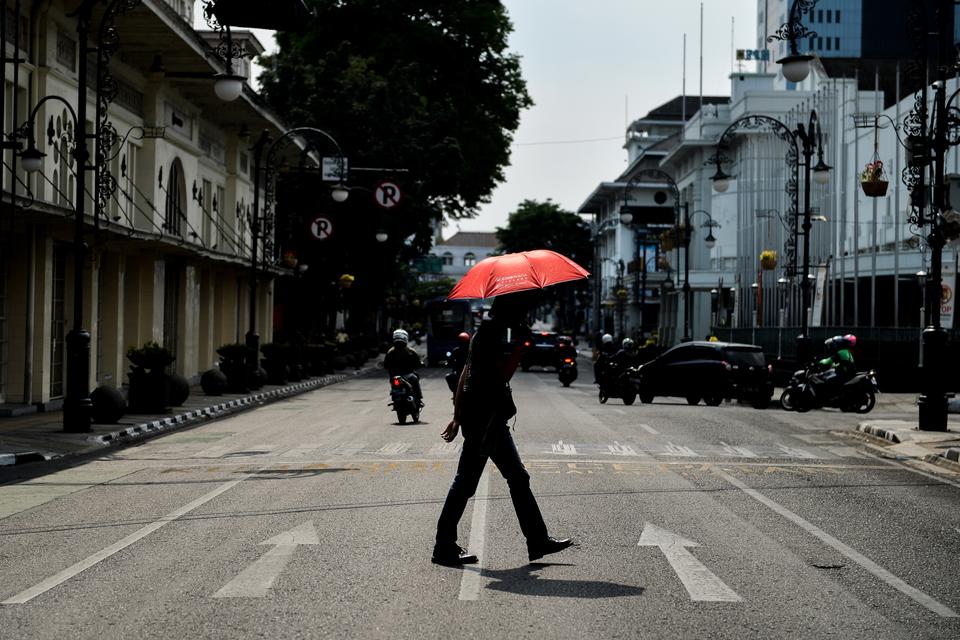 Warga mengenakan payung saat menyeberangi Jalan Asia Afrika, Bandung, Jawa Barat, Rabu (18/10/2023). 