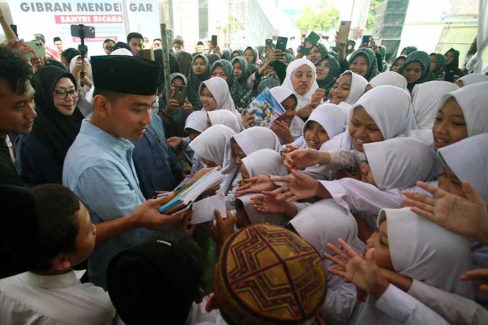 Calon wakil presiden nomor urut 2 Gibran Rakabuming Raka (kedua kiri) membagikan buku tulis kepada para santri saat mengunjungi Pondok Pesantren Asshidiqiyah Tangerang, Banten, Senin (4/12/2023). Dalam kunjungan tersebut Gibran mengajak para santri mengik
