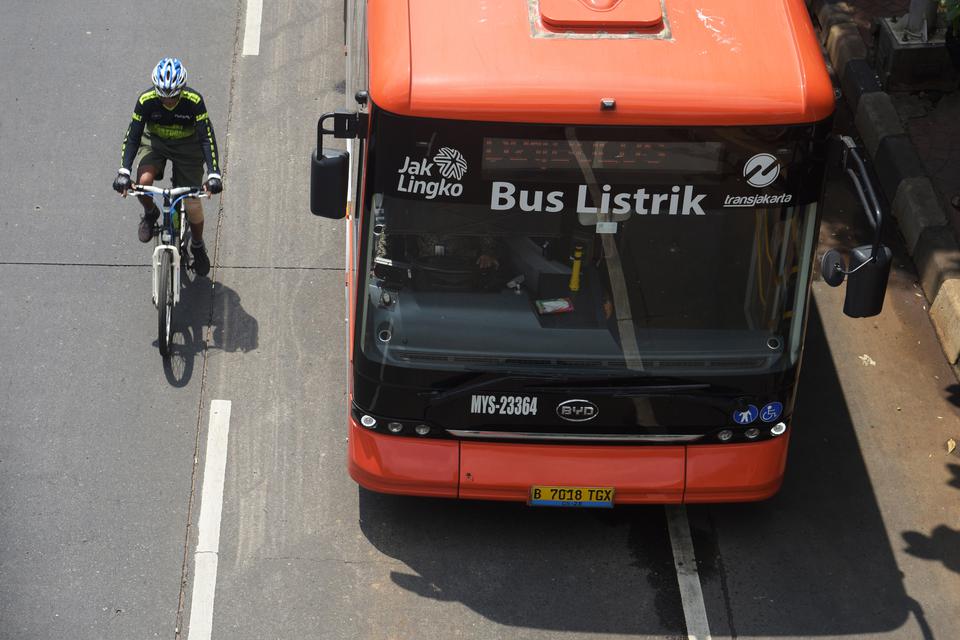 Pengendara sepeda melaju di samping bus listrik Transjakarta di halte bus Universitas Indonesia, Depok, Jawa Barat, Minggu (31/12/2023). Penggunaan bus berbasis listrik itu menjadi salah satu langkah nyata untuk mencapai net zero emisi serta mewujudkan tr