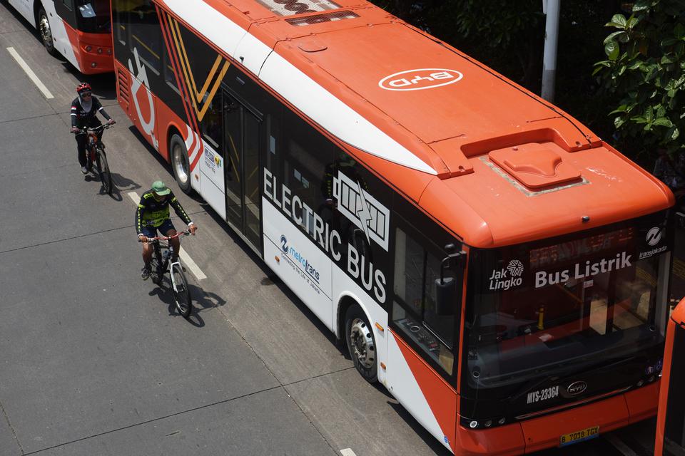 Pengendara sepeda melaju di samping bus listrik Transjakarta di halte bus Universitas Indonesia, Depok, Jawa Barat, Minggu (31/12/2023). Penggunaan bus berbasis listrik itu menjadi salah satu langkah nyata untuk mencapai net zero emisi serta mewujudkan tr
