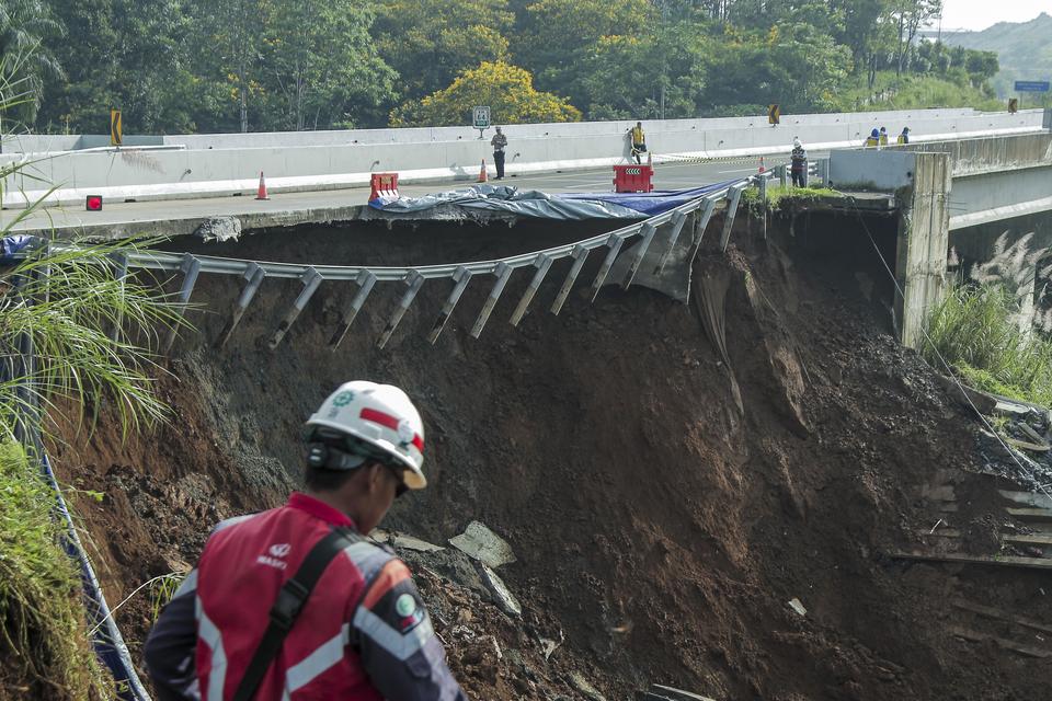 Petugas melintas di sekitar jalan tol yang amblas di ruas tol Bocimi KM 64, Sukabumi, Jawa Barat, Kamis (4/4/2024). Jalan tol Bocimi KM 64 yang amblas pada Rabu (3/4) malam tersebut mengakibatkan satu mobil dan dua orang terperosok dan arus lalu lintas da