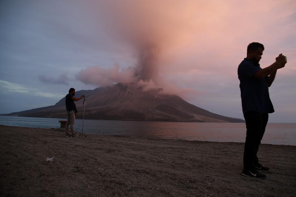 Dua orang jurnalis mengabarkan kondisi Gunung Ruang saat erupsi terlihat dari Pelabuhan Tagulandang, Kabupaten Kepulauan Sitaro, Sulawesi Utara, Rabu (1/5/2024). 