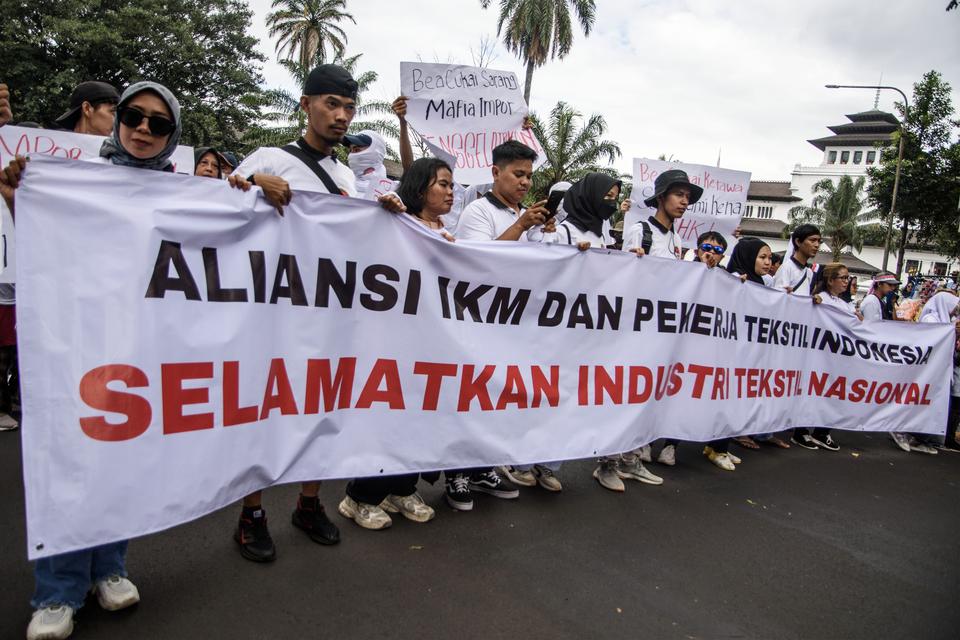 Massa yang tergabung dalam Aliansi IKM dan Pekerja Tekstil Indonesia membentangkan spanduk saat berunjuk rasa di depan Gedung Sate, Bandung, Jawa Barat, Jumat (5/7/2024).